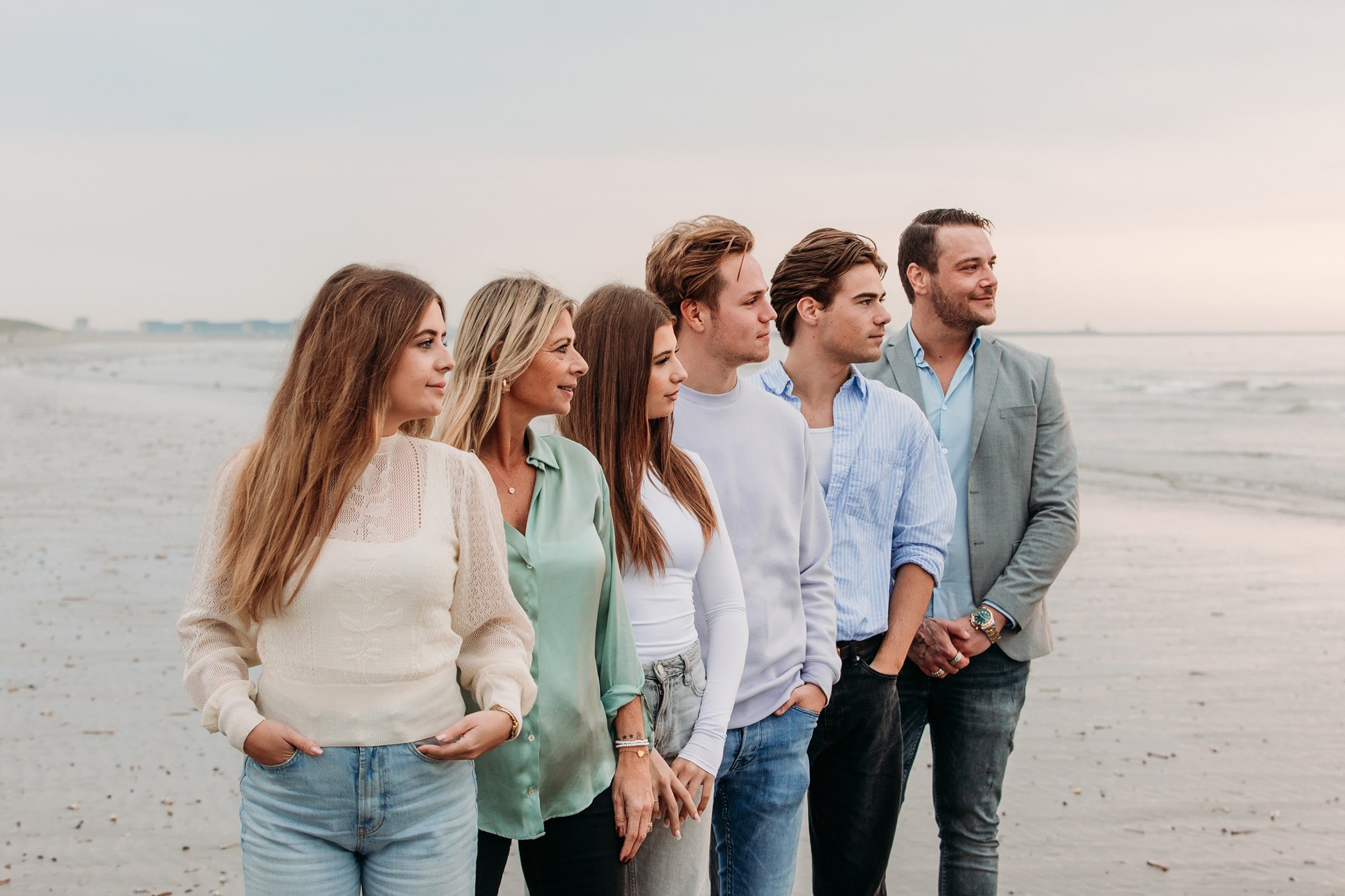 Familie van vijf staand naast elkaar op het strand