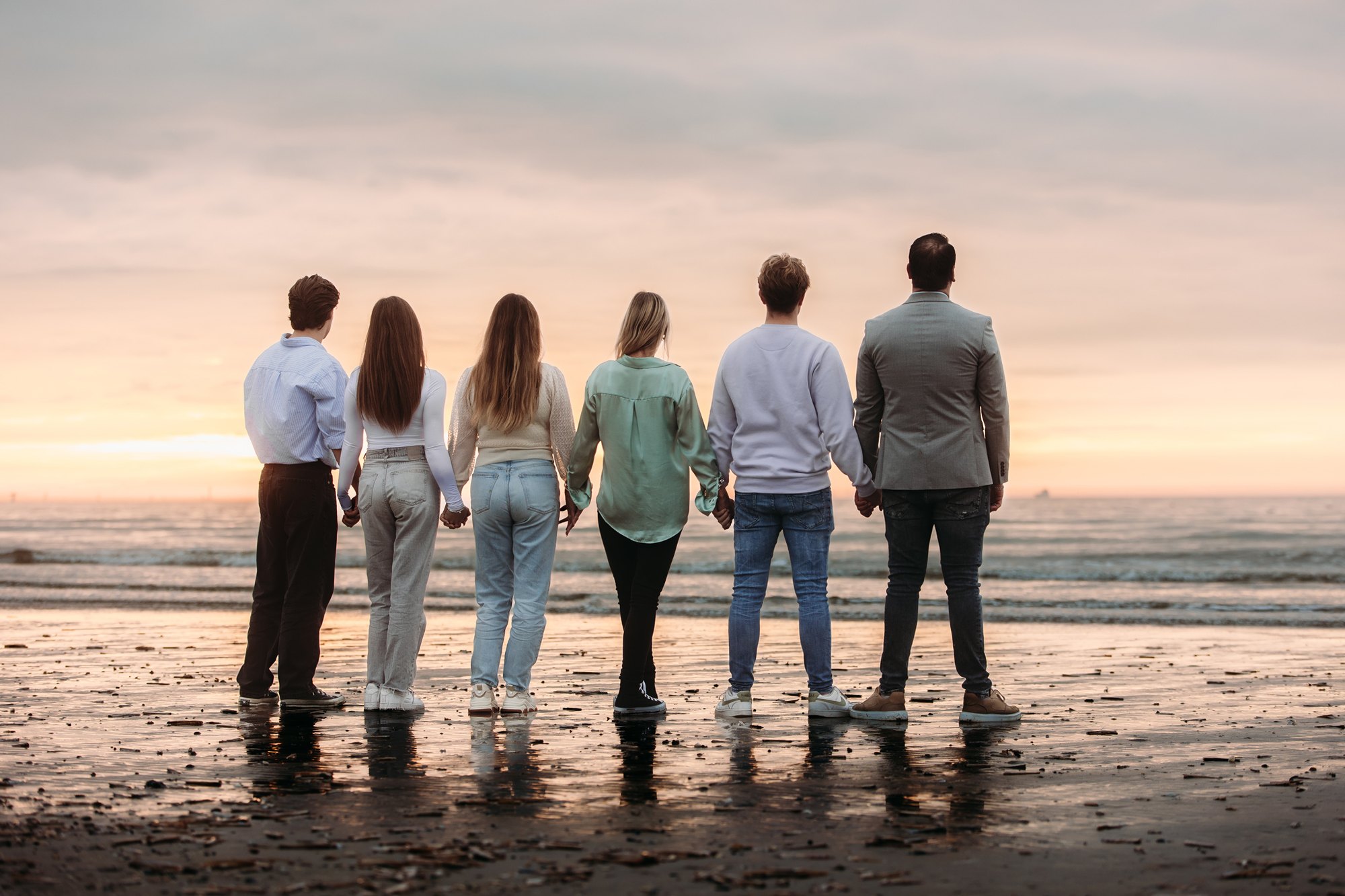 Familie van achteren gefotografeerd op het strand tijdens zonsondergang